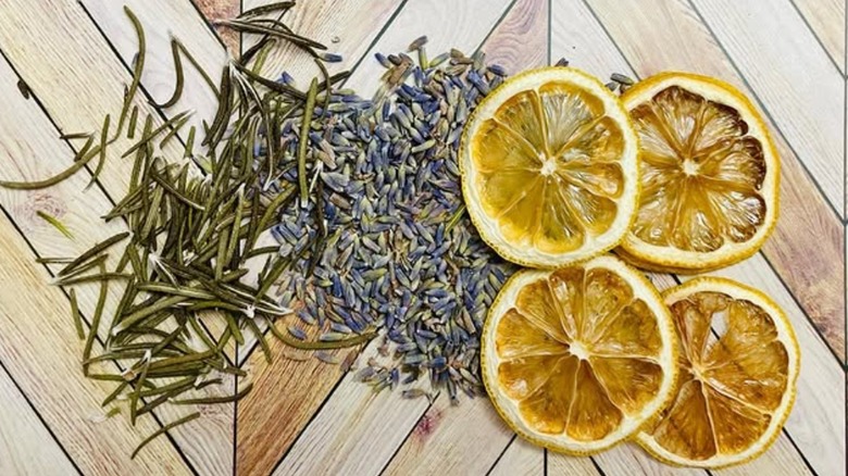 Rosemary leaves, dried lavender, and lemon slices are spread out on a wooden surface.
