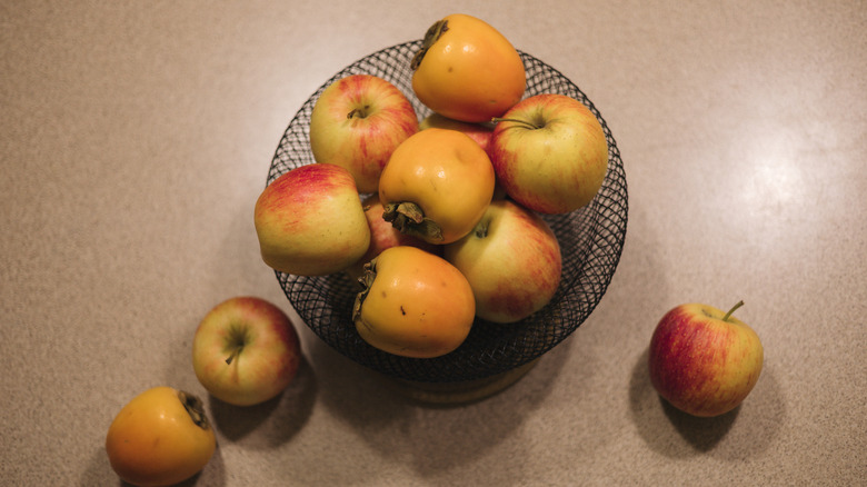 Apples and persimmons in basket on table