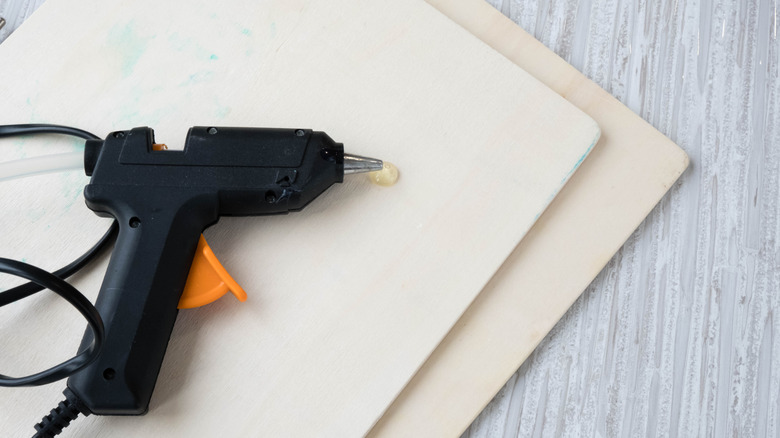 A hot glue gun laying on a piece of wood with a little puddle of melted glue below.