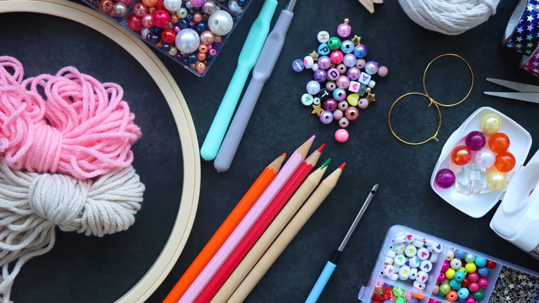 A range of craft supplies on a black table, including yarn, beads, pencils and crochet hooks