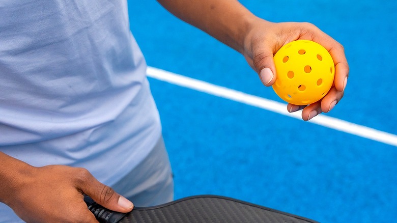 Close-up of a person holding pickleball and paddle on a blue pickleball court