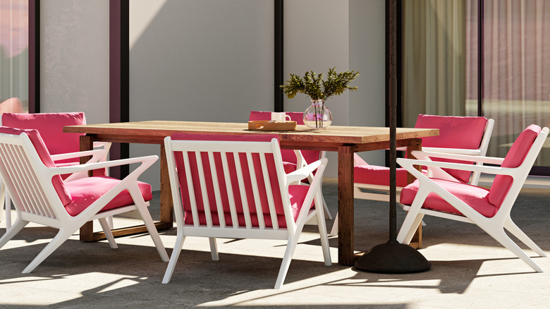 White chairs with pink cushions surround a wooden table on an outdoor patio