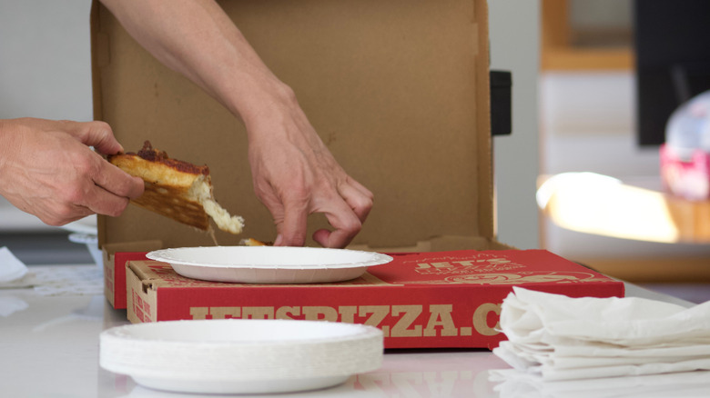 Someone taking a slice of pizza out of a cardboard pizza box.