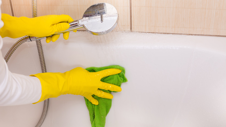 Yellow gloved hands cleaning bathtub.