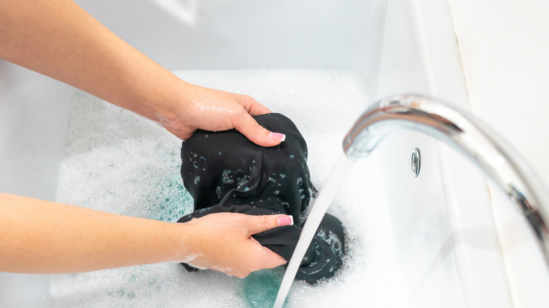 Woman washing black clothing in sink.
