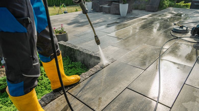 Man in yellow boots washing patio.