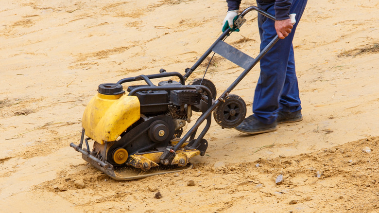 A man using a pate compactor on the sand for a patio sub-base