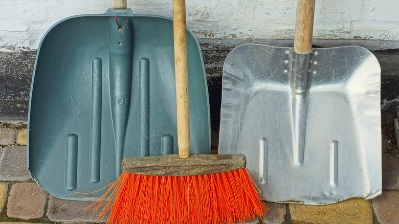 Plastic and metal snow shovels with broom in between