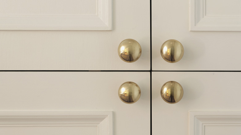 Four polished brass cabinet pulls on white cabinet doors