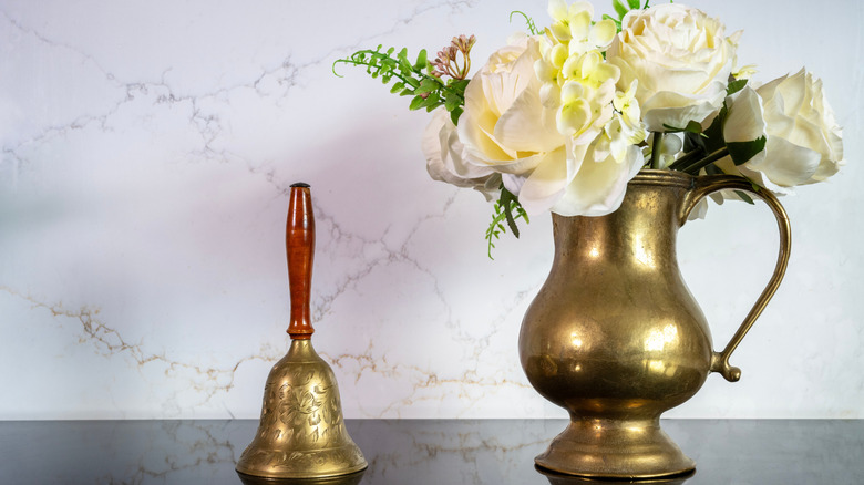 A polished brass vase pitcher and bell on a countertop