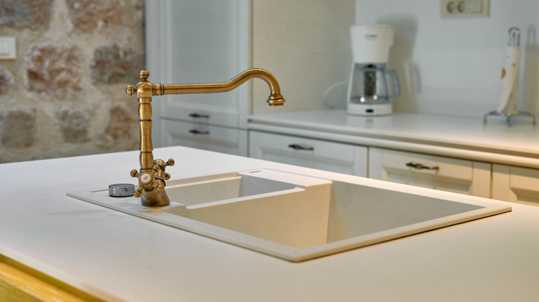 A sink with a brass faucet in a kitchen with white counters