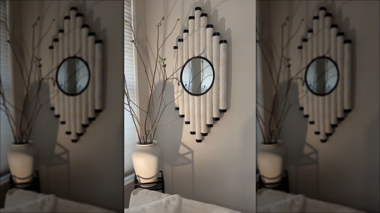 A pool noodle mirror DIY on a wall with whitish coloring and black accents with a round mirror in the center
