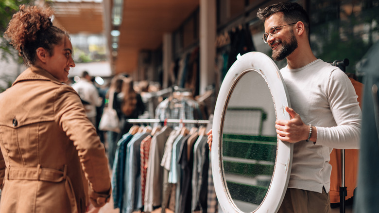 A man holds up an old circular mirror at a thrift store