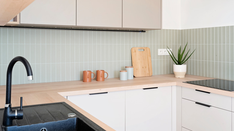 A modern kitchen with a light green tile backsplash and minimal decor