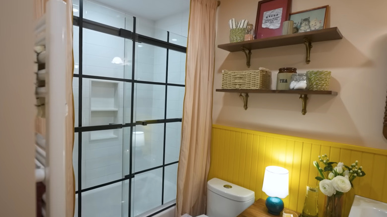 a colorful small bathroom makeover with yellow panels behind the toilet and pink curtains enclosing a glass shower