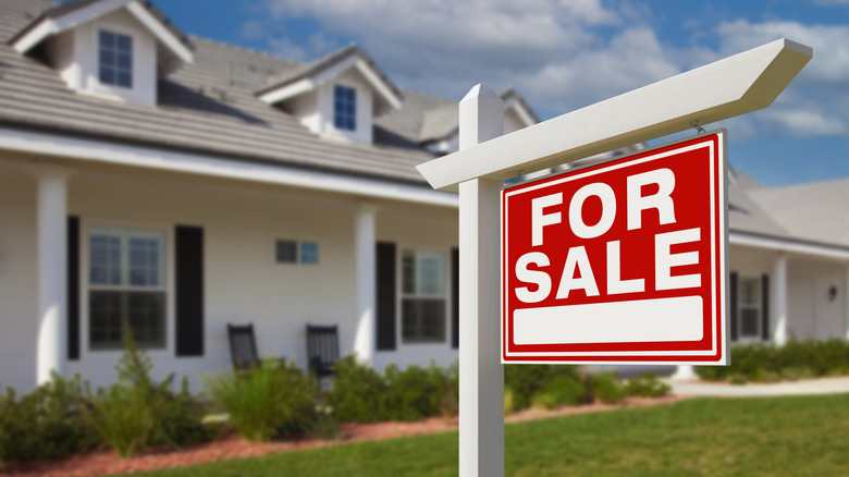 white house with black shutters and for sale sign