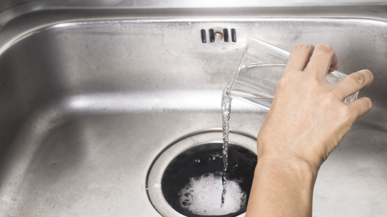 Someone pouring a glass of white vinegar in kitchen sink drain
