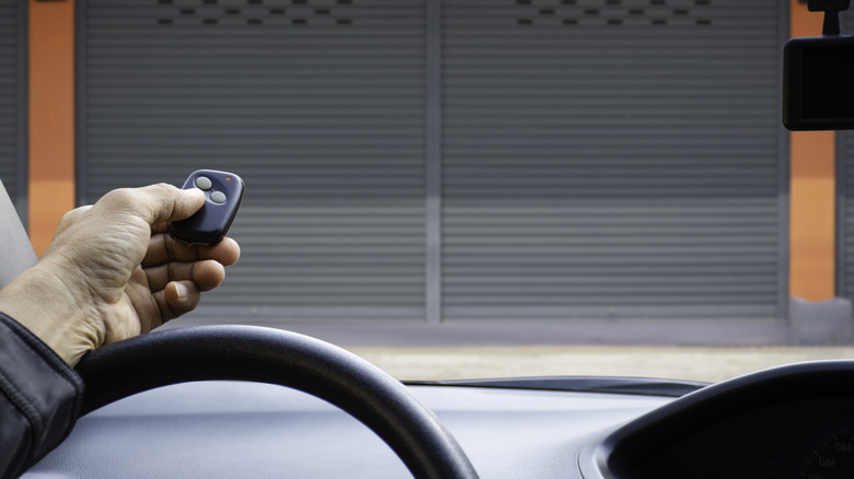 Hand pointing a small black remote at a gray garage door
