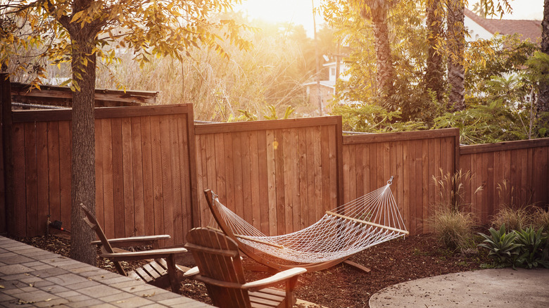 A sunny backyard with a fence, hammock, and chairs.