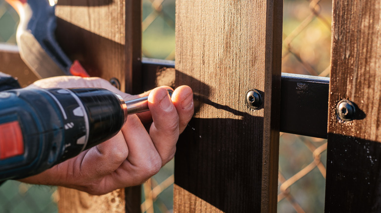 Drilling a wood panel onto a fence