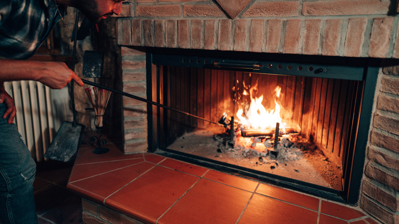A man pokes a fire in a stone fireplace