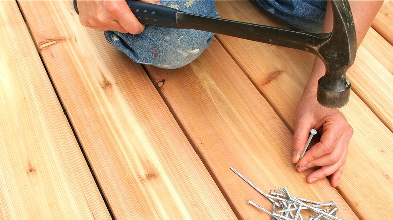 Person nailing nail in deck