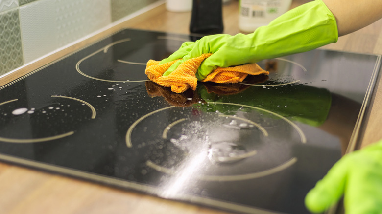 Person wiping down a glass stovetop while wearing a glove