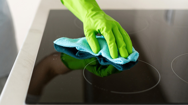 Gloved hand cleaning ceramic glass stovetop