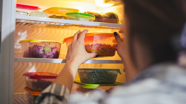 A person taking a container out of an open fridge