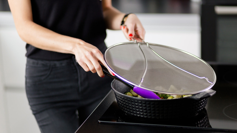 A person cooking while holding a splatter screen over the frying pan.