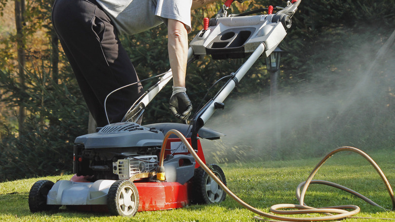 Someone cleaning out their lawn mower deck with a hose.