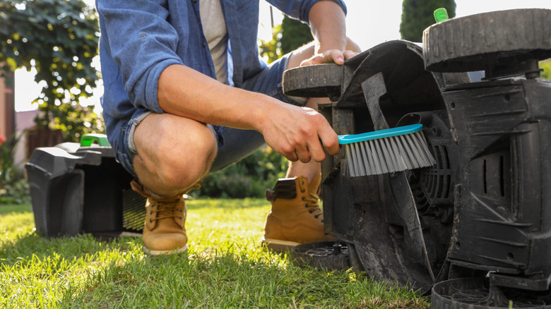 Person cleaning a lawn mower blade with a brush