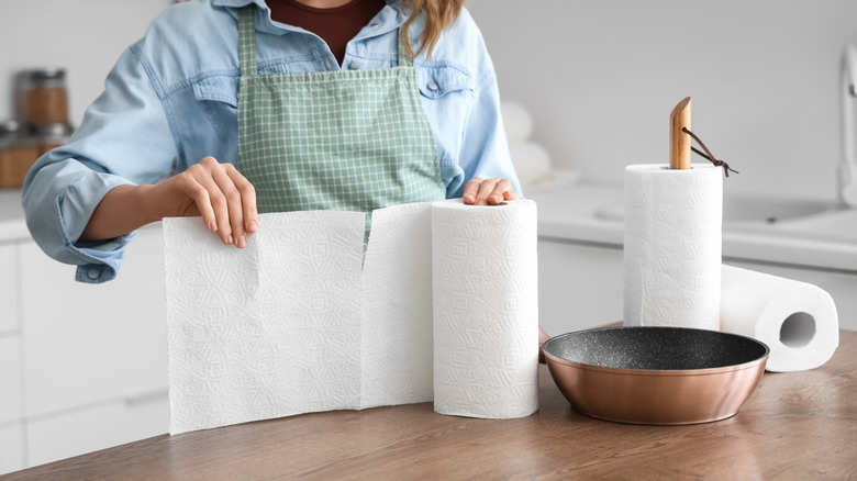 Woman pulling paper towel beside cooking pan