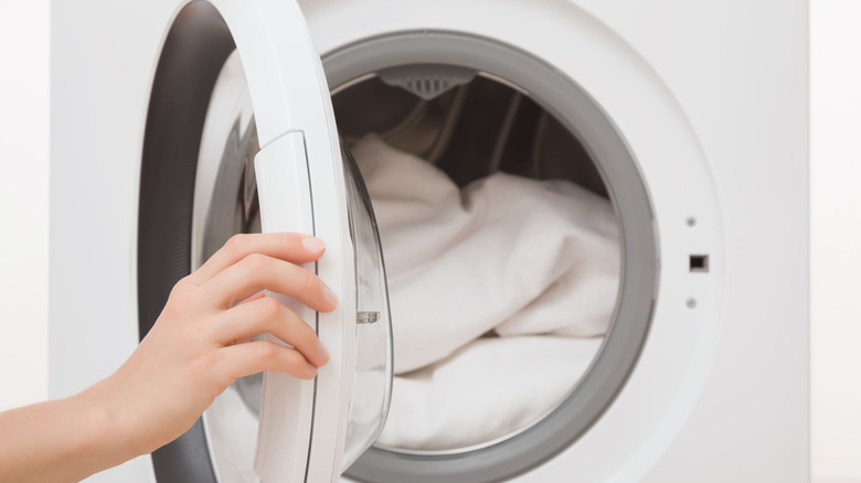 Woman opening white dryer with white sheets inside
