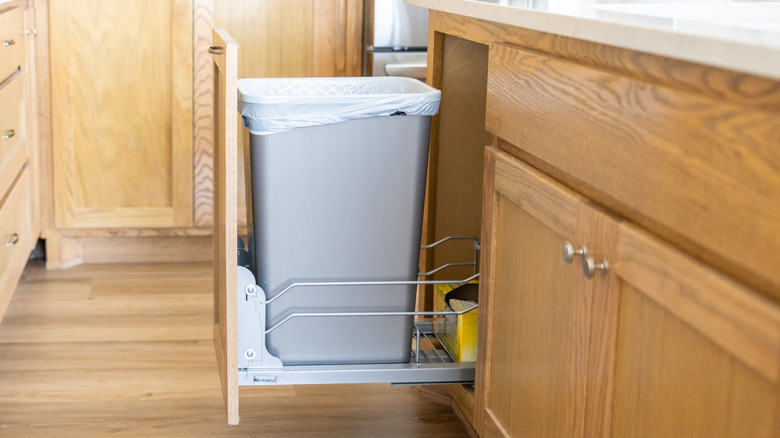 A pull-out kitchen trash cabinet in a modern wood-finished kitchen.