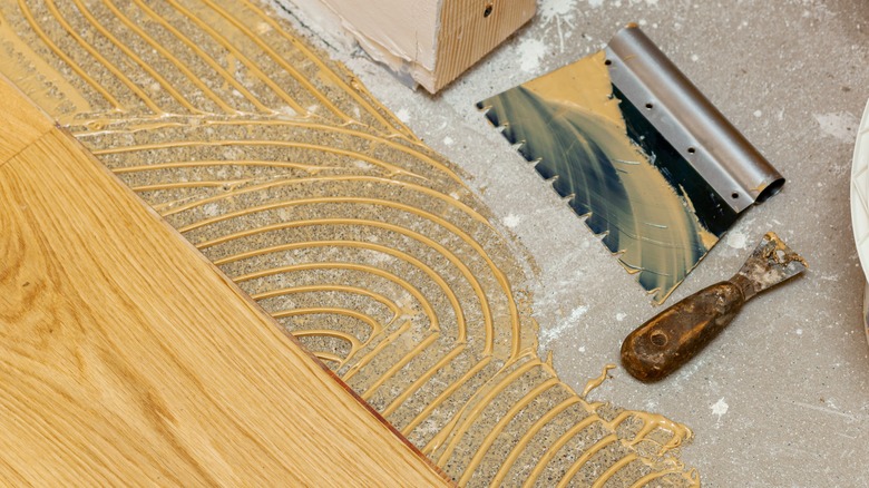 A cleaned-off trowel sits next to freshly applied wood glue and flooring planks