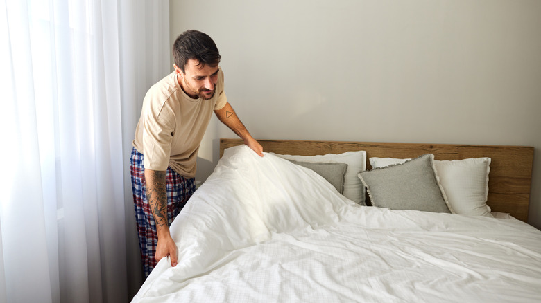 A man pulls a comforter up on a bed as he makes it.
