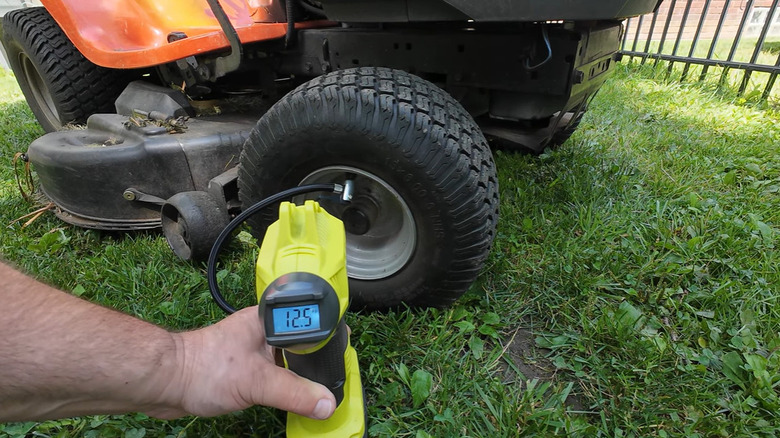 Someone checking the air pressure of a lawnmower tire