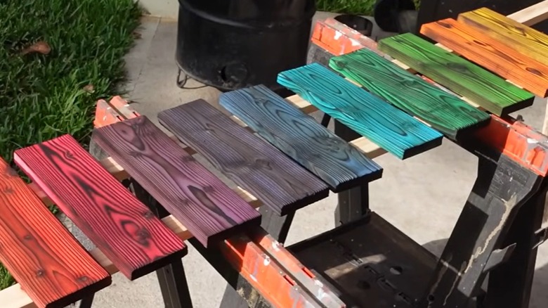 A row of shou sugi ban wood pieces are dyed an array of colors with food coloring and water.
