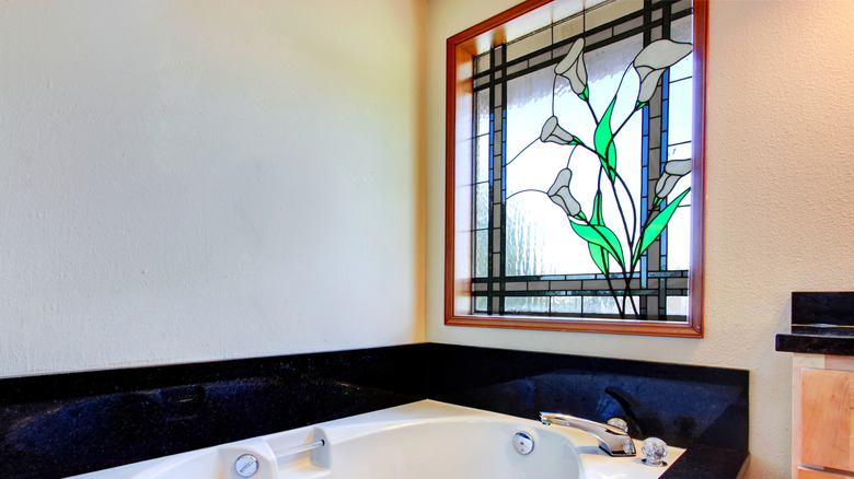 Bathroom with white whirlpool tub, black tile trim around it and stained glass window