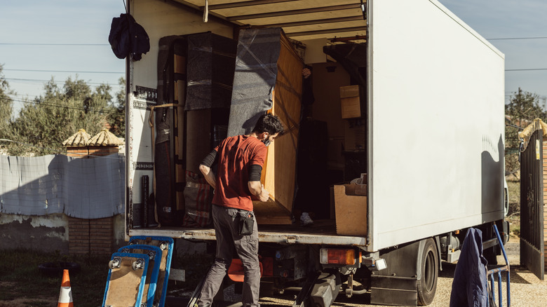 Two movers using a moving blanket to put furniture into a van