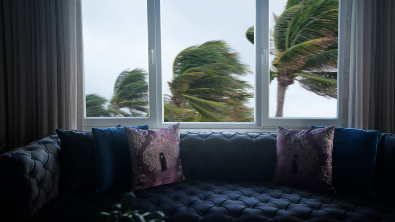 View from a living room out the window of a tropical storm blowing palm trees.
