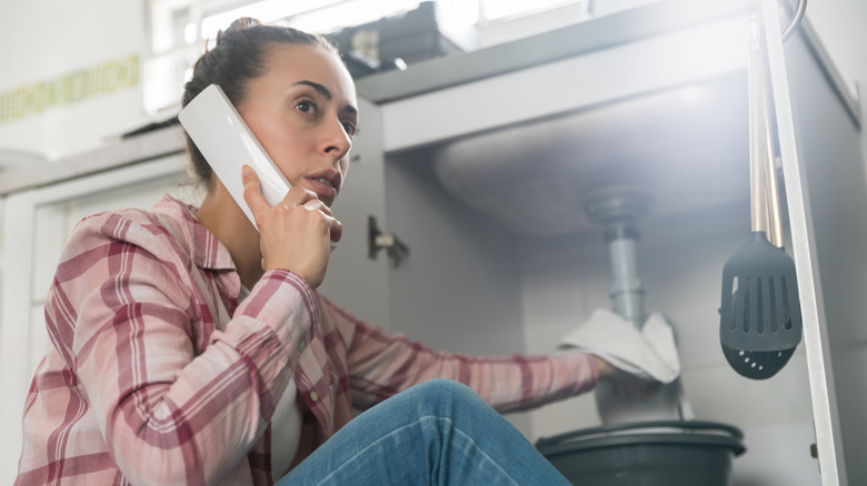 woman at home calling a plumber about a leaking pipe in her sink