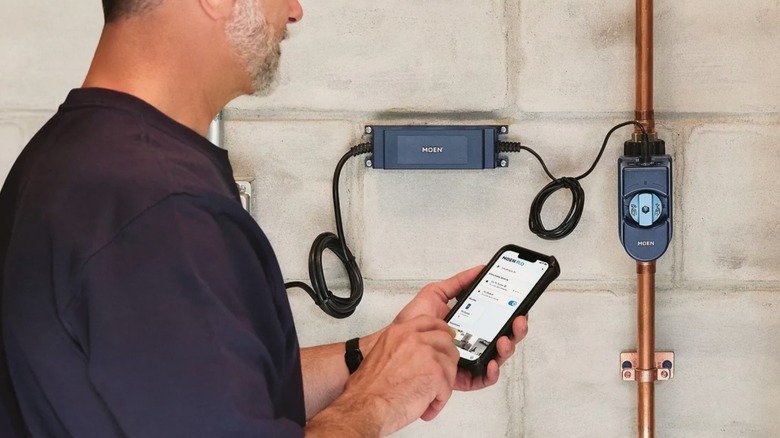a person using the Moen Flo Shutoff app in front of the Mown Flo Shutoff device