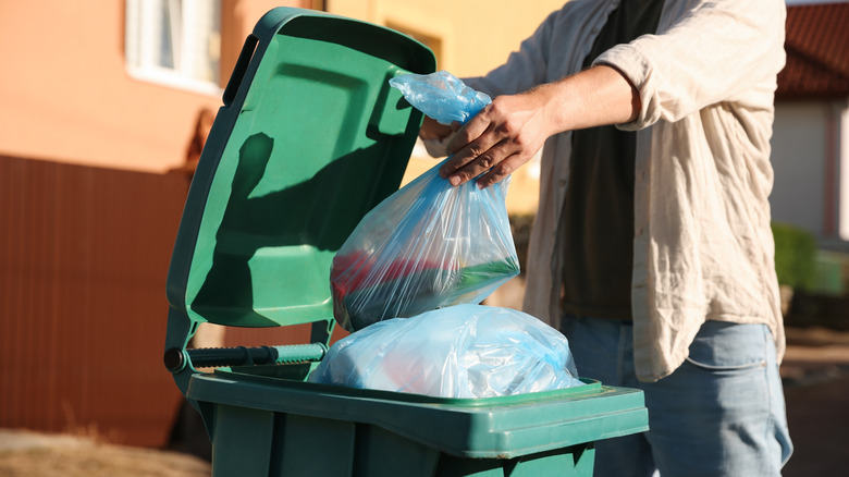 Person throwing garbage bag into a green outdoor bin