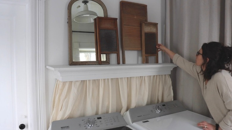 Person decorating shelf over washer and dryer with valance curtain hiding hookups