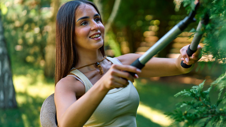 Woman holding pruning shears up to prune a plant.