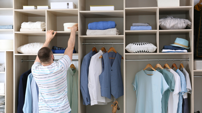 A man stretches to reach a box high up in a closet.