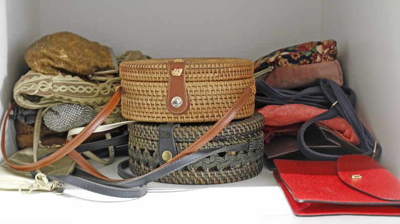 Handbags of various color and material, including vintage and woven, shoved in a closet in a pile