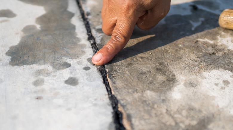 man pressing on rubber sealant in between concrete payament